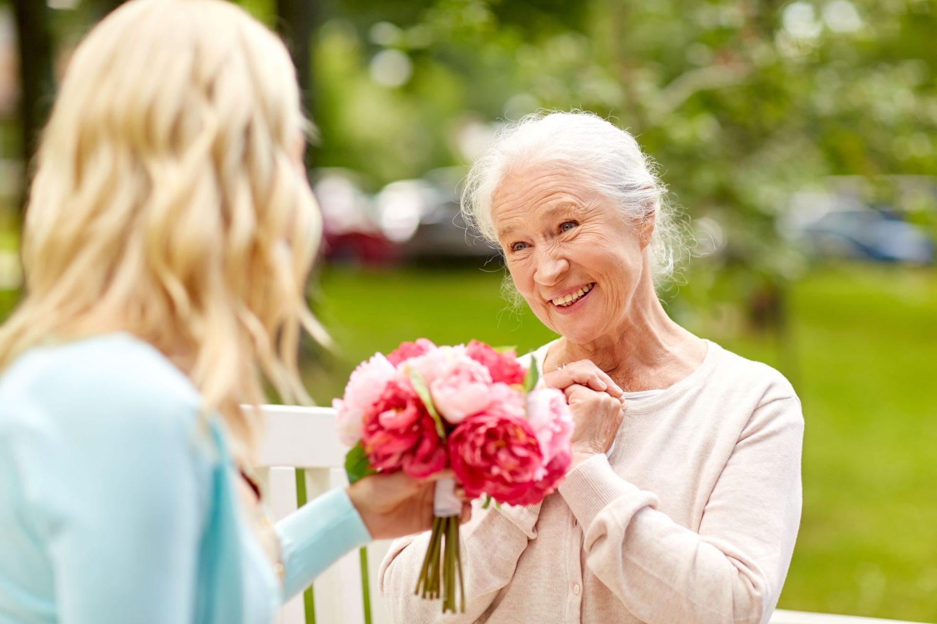 senior woman smiling while receiving flowers from another woman