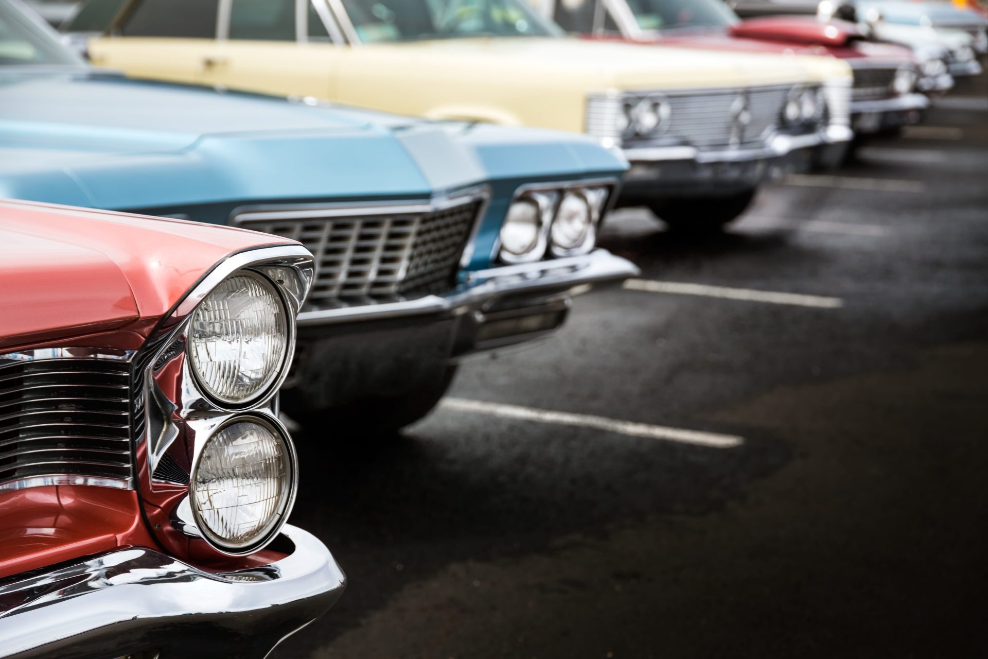 Close-up view of classic cars lined up in a parking lot, showcasing colorful vintage designs.